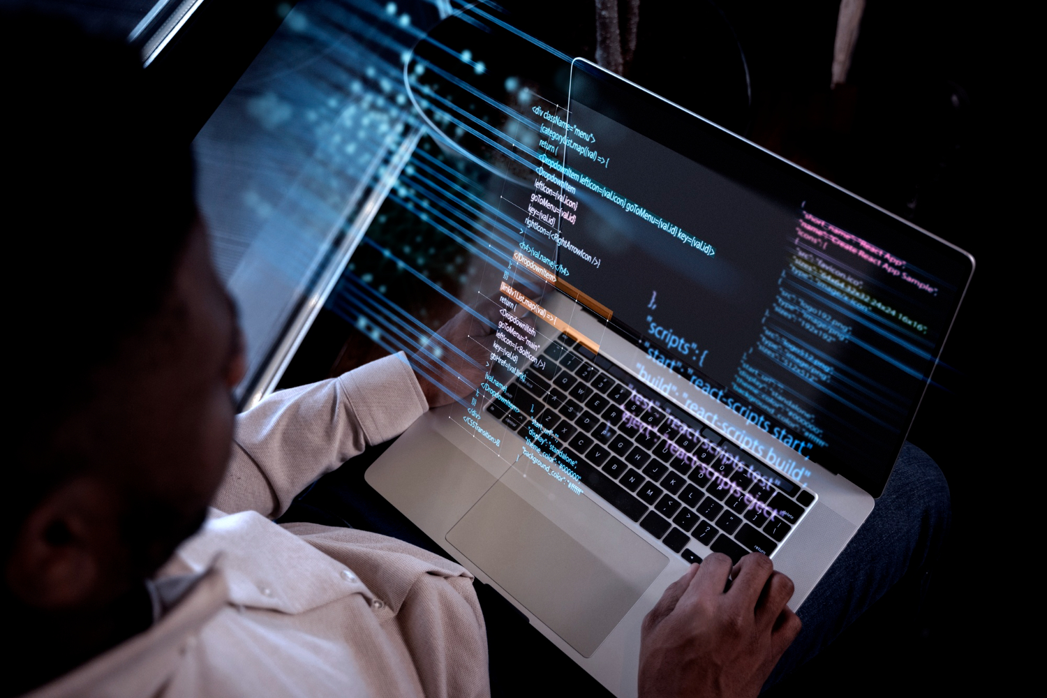 homem com laptop no colo programando, na tela mostrando codigos em neon